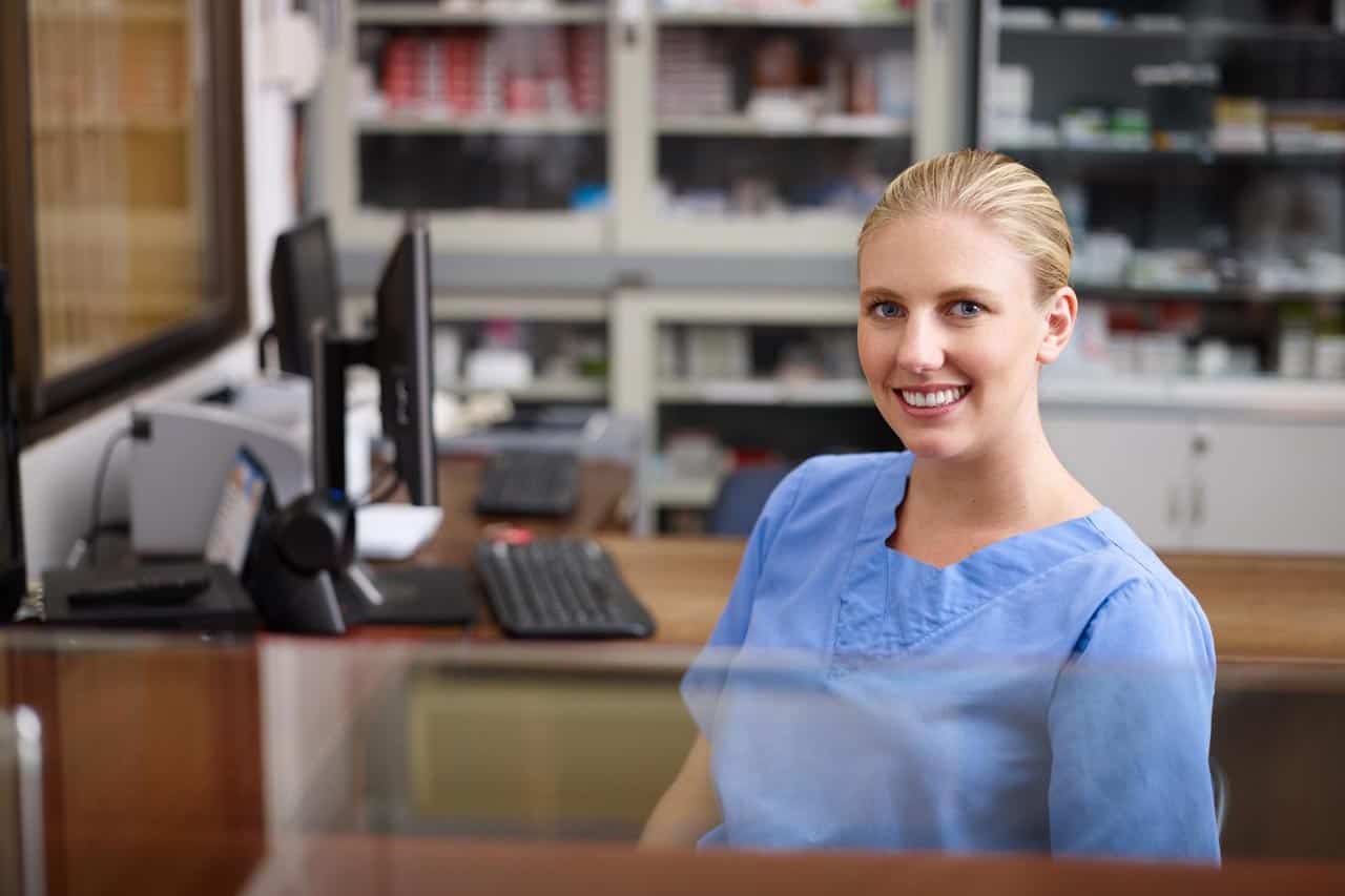 Young woman at work as receptionist and nurse in hospital, looking at camera