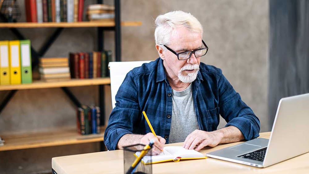 Mature man taking notes at laptop