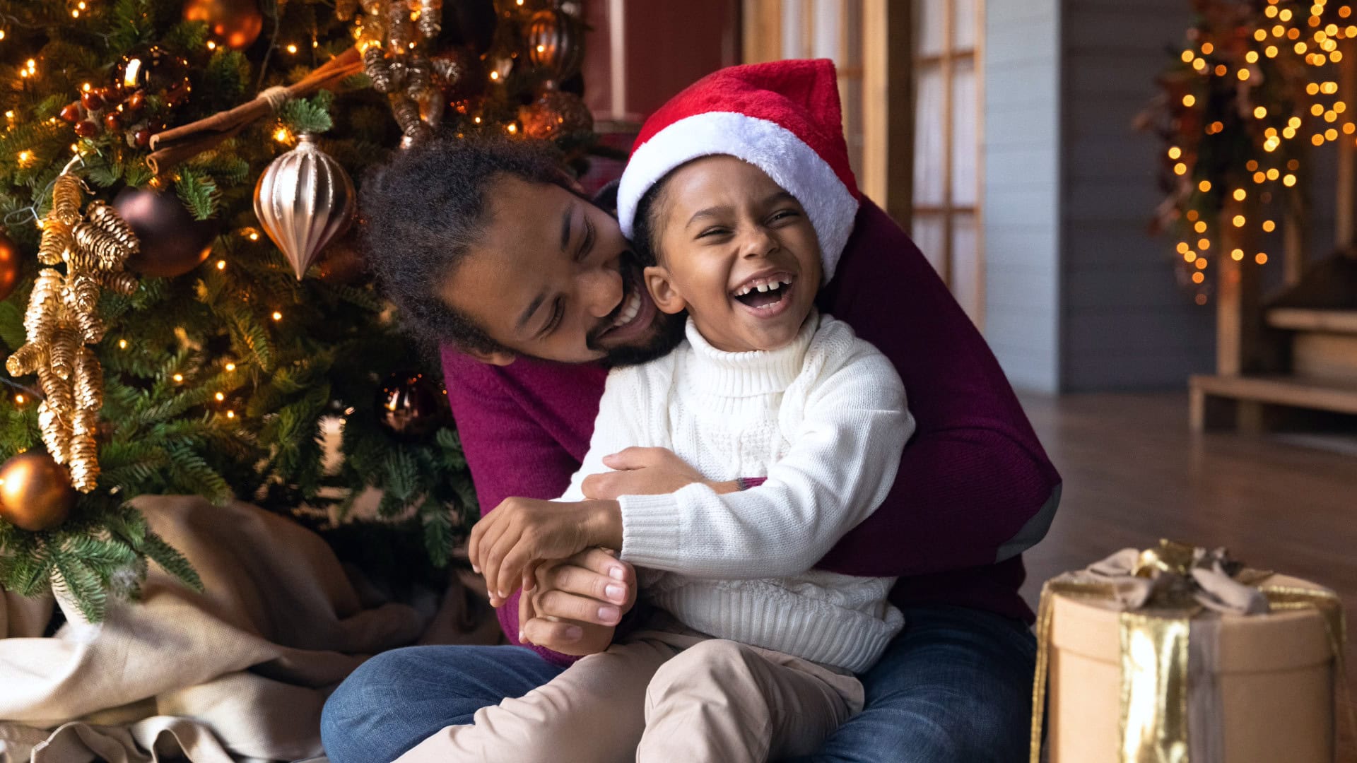 Father and daughter wearing Santa hats and cuddling by the Christmas tree. 
