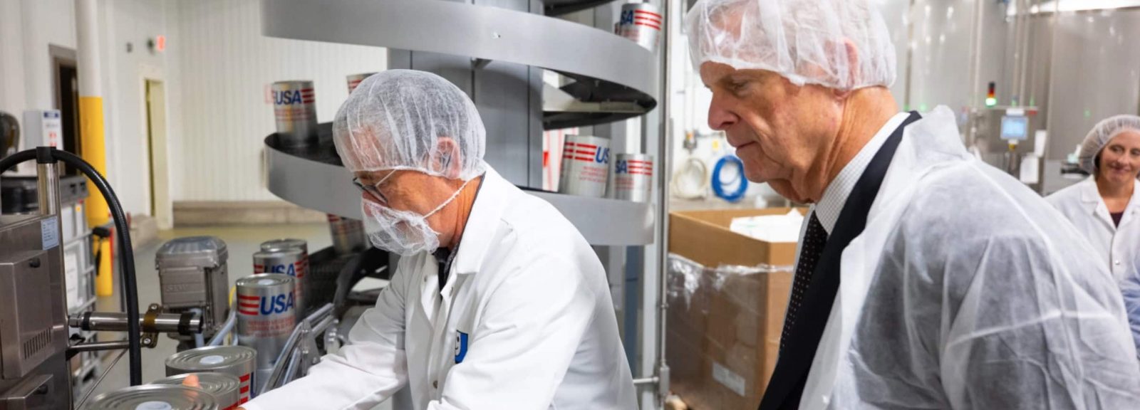 Former Iowa Gov. and U.S. Secretary of Agriculture toured Goodwill's Oil Packaging Plant in Coralville during June 2026. In this photo, Plant Director Spike Stabler demonstrates the production line where soybean oil is fortified before being packaged and shipped to combat hunger.