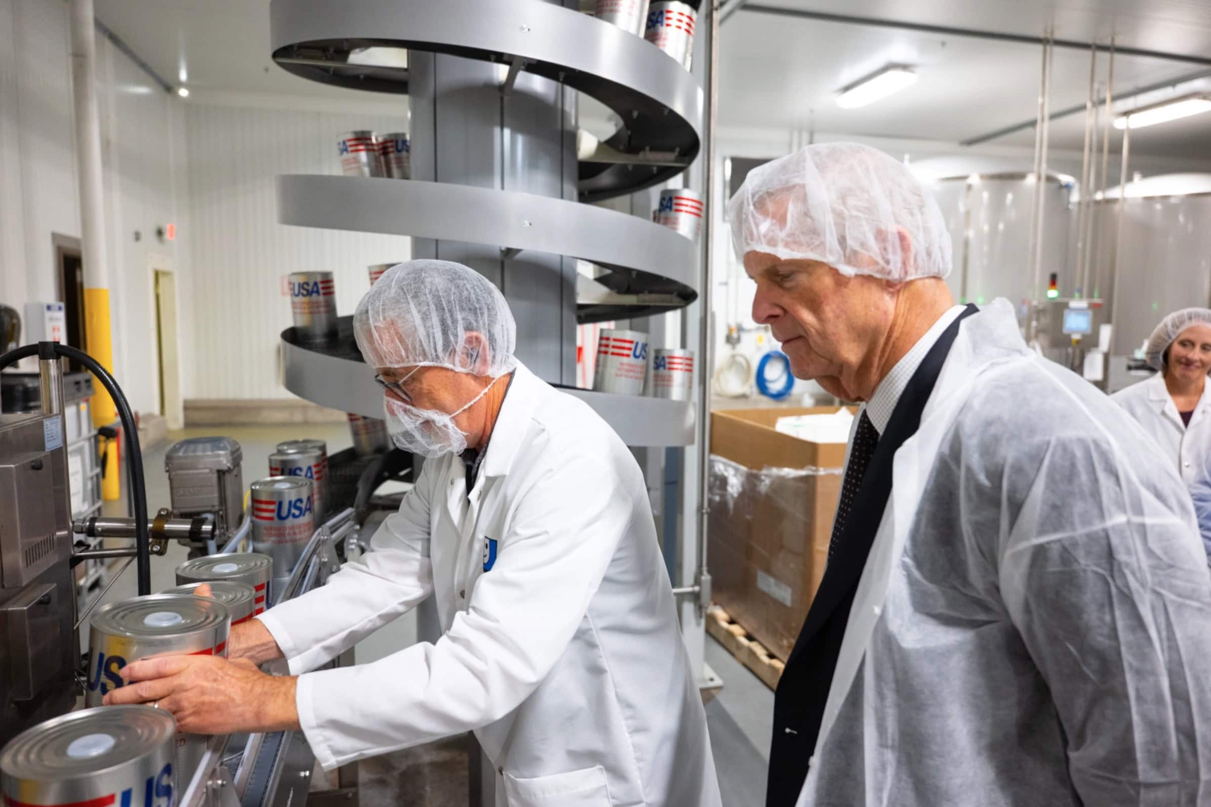Former Iowa Gov. and U.S. Secretary of Agriculture Tom Vilsack toured Goodwill's Oil Packaging Plant in Coralville during June 2026. In this photo, Plant Director Spike Stabler demonstrates the production line where soybean oil is fortified before being packaged and shipped to combat hunger. 